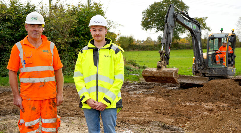 Two white men in hi-vis safety gear stand at a construction site