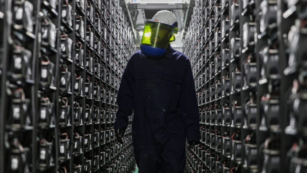 A man in a full face protective mask stands between battery storage systems
