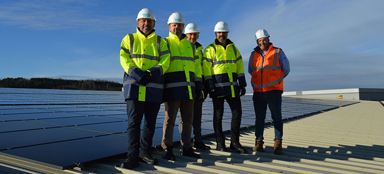 Men in hard hats stand near a rooftop solar panel