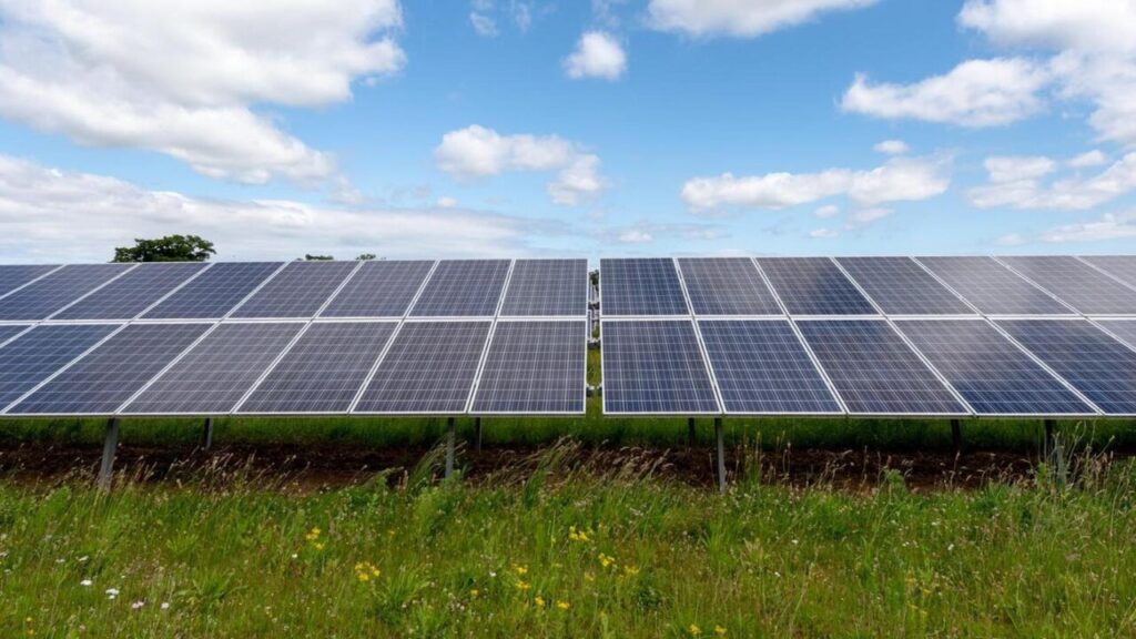 solar panels with blue sky and clouds above and green grass below