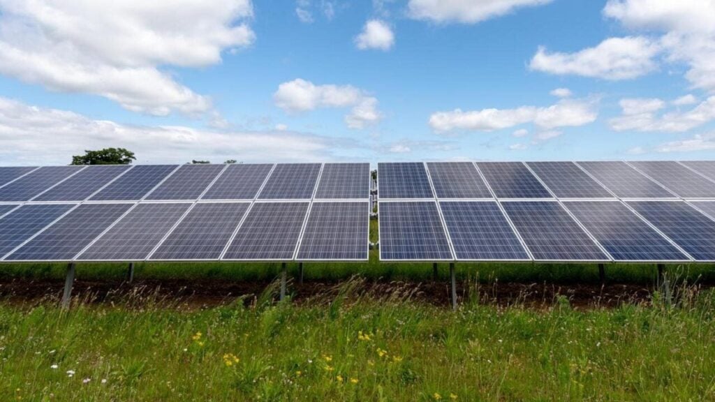 solar panels with blue sky and clouds above and green grass below