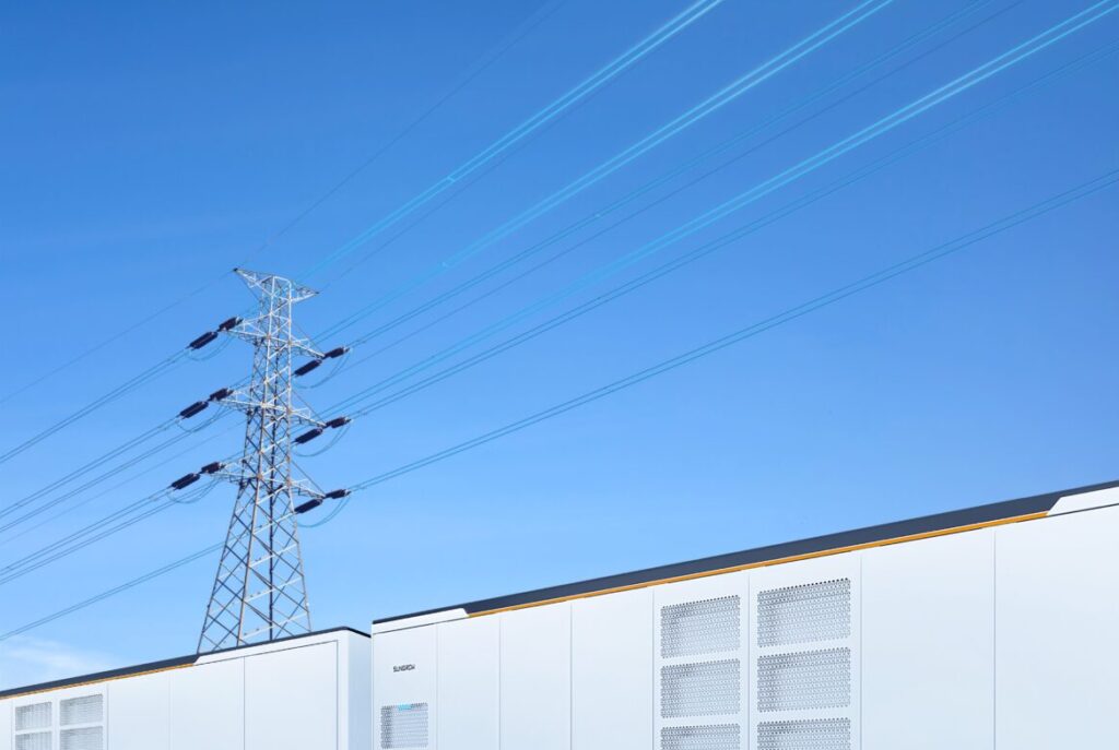 White BESS units underneath a blue sky with a pylon and electricity wires above