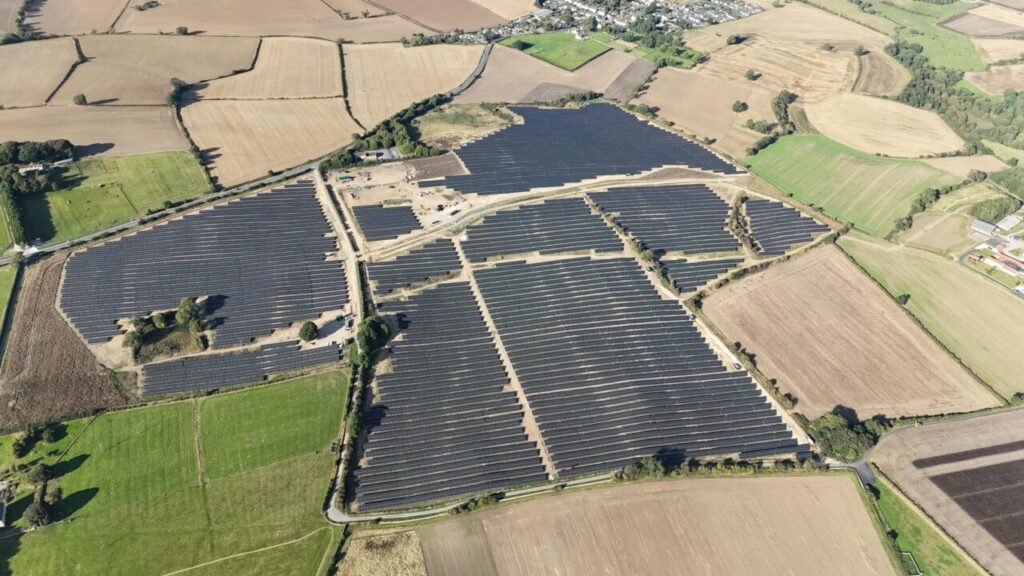 An overhead photograph of a large solar farm situated among green fields