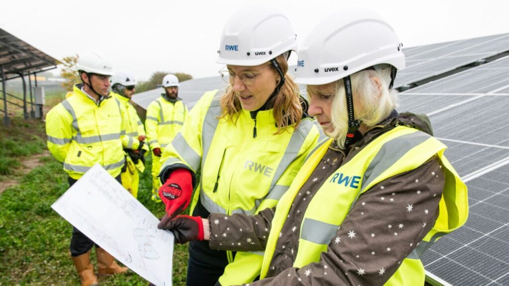 Two women look at a clipboard in front of solar panels