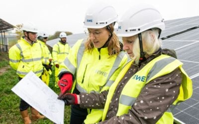 Two women look at a clipboard in front of solar panels