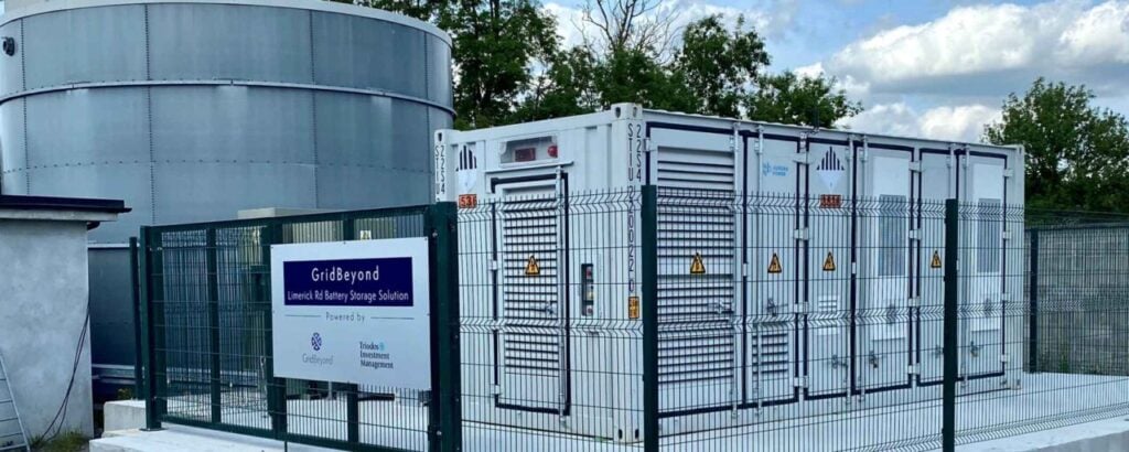 BESS units behind a metal fence with a sign bearing the Triodos and GridBeyond logos